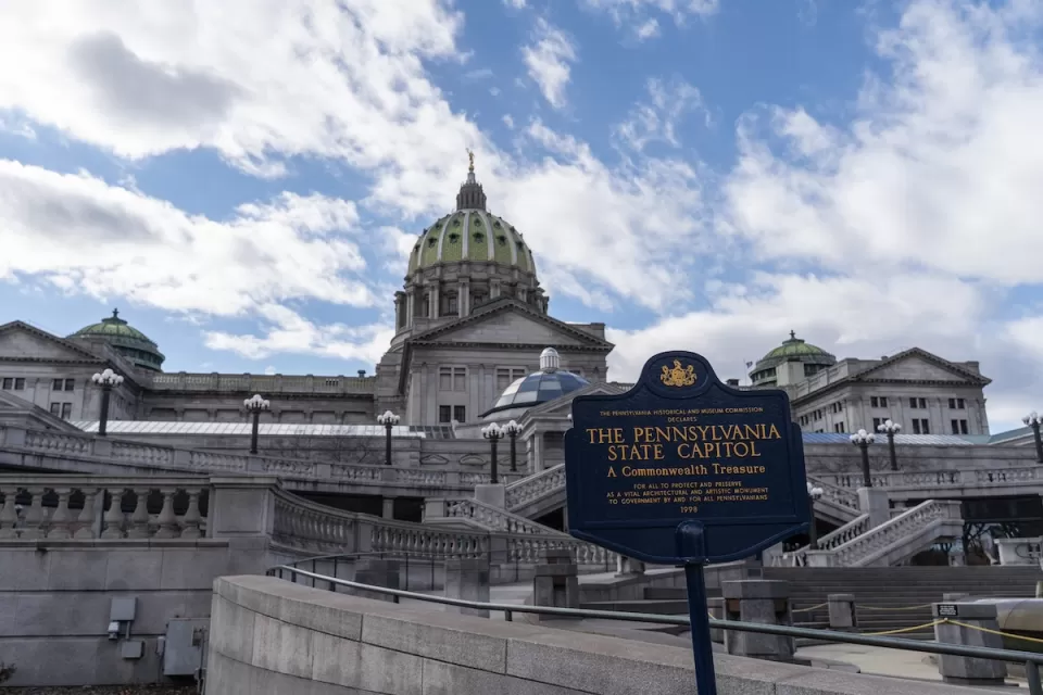 View of Pennsylvania state capitol building with historical plaque in foreground.